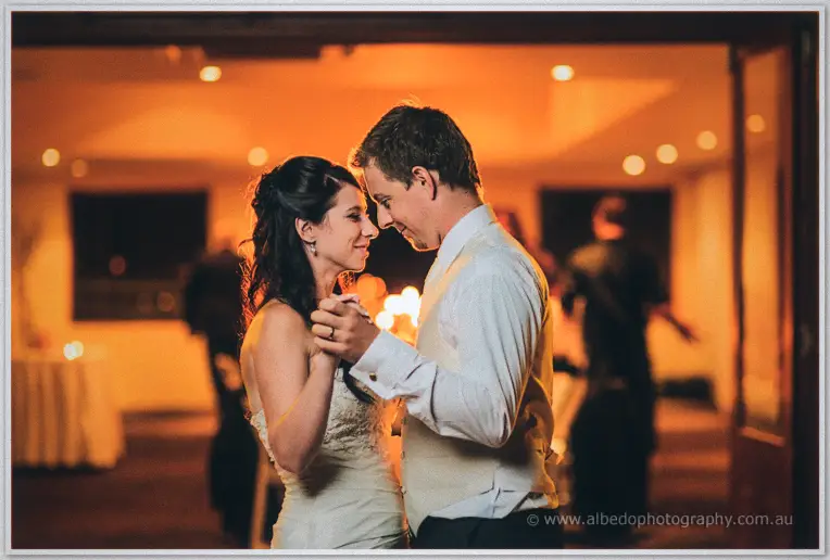 Foreheads touching, the couple hold hands mid-dance in the amber glow of the reception room.