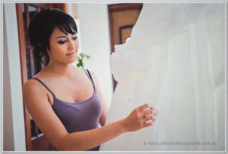 Bride Sarah in a lilac camisole reaching to touch the ruffled tulle of her hanging gown