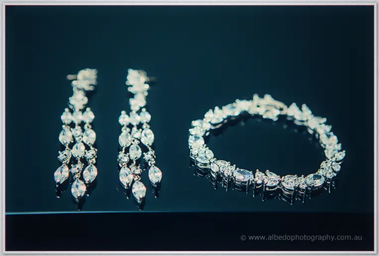 Sarah's chandelier earrings and crystal bracelet glinting on a dark reflective surface