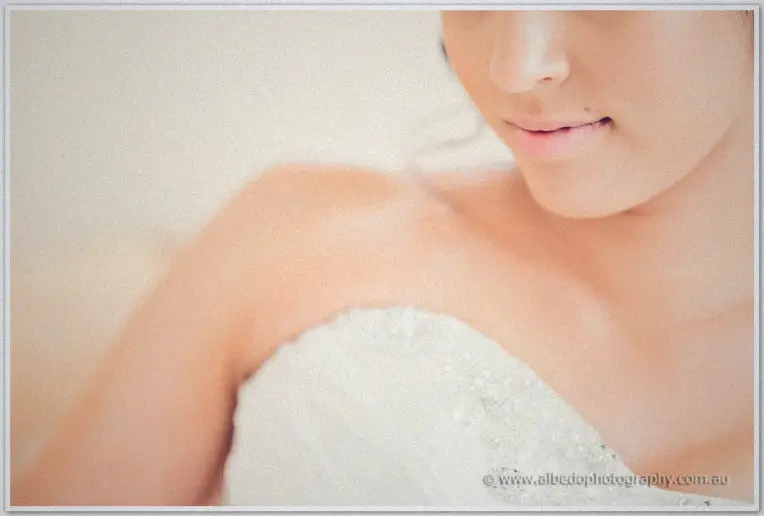Intimate close-up of Sarah's bare shoulder and beaded gown edge, warm light on her calm face