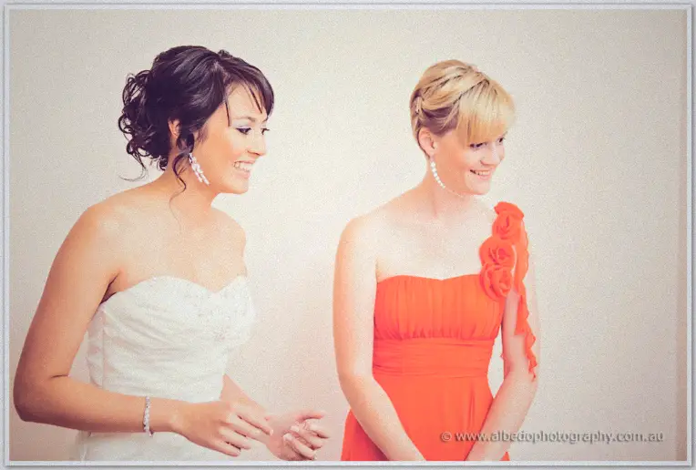 Bride Sarah in her strapless gown laughing with a bridesmaid in an orange rose-shoulder dress