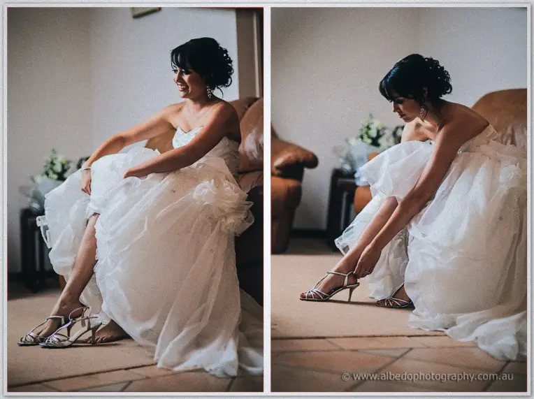 Bride Sarah seated on the couch stepping into her silver heels, her ruffled gown pooling around
