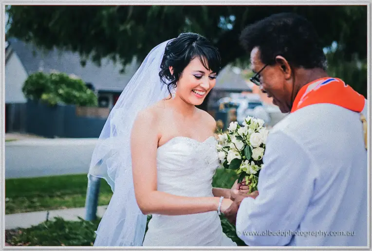 Bride Sarah arriving breathless and laughing as the priest greets her by the church steps