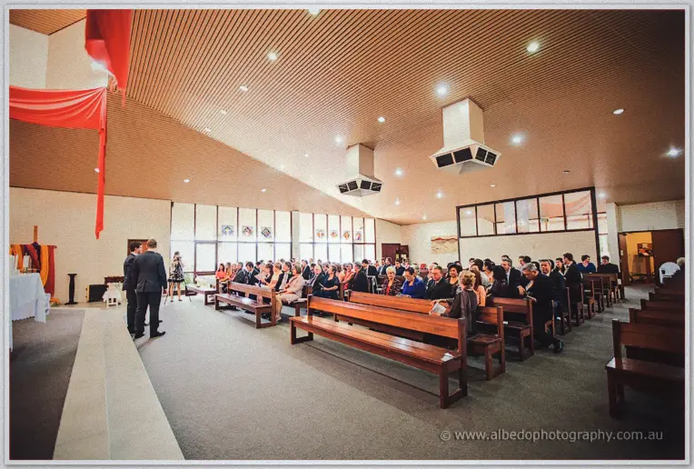 Wide view of the timber-ceilinged church filled with guests as the priest waits at the front
