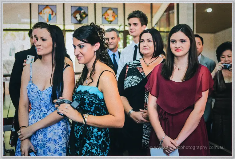 Wedding guests in the church foyer watching the ceremony, one filming on a small handheld camera