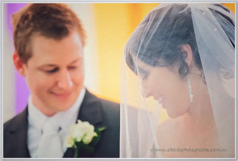 Split close-up of groom Shannon smiling down and bride Sarah laughing beneath her veil, golden light
