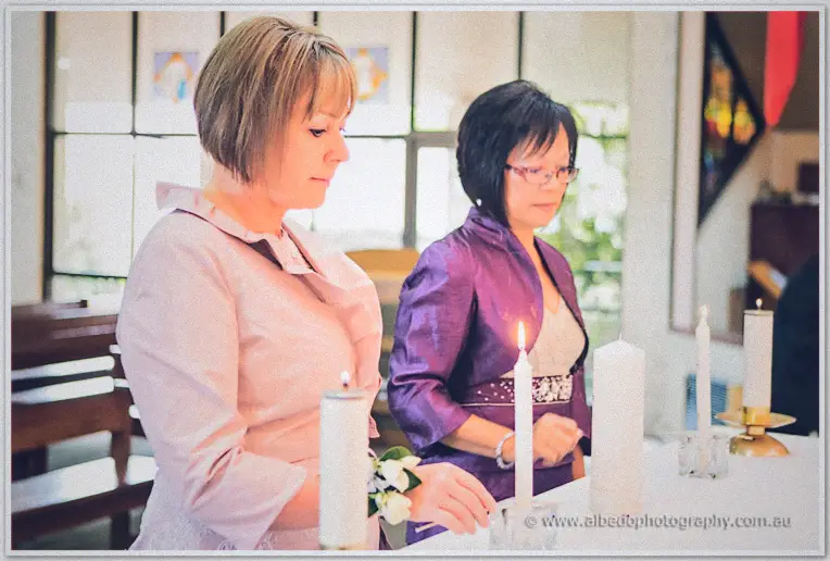 Two mothers lighting the taper candles at the ceremony table in pink and purple jackets