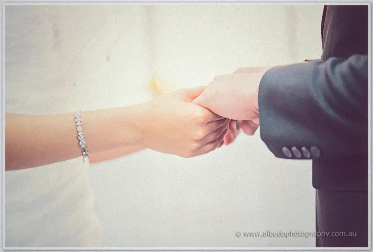 Close-up of Sarah's crystal-braceleted hand clasping Shannon's as they join hands at the altar
