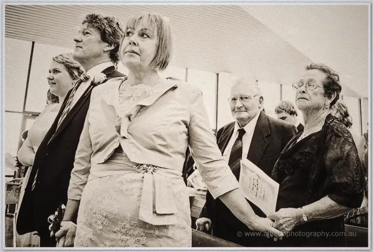 Sepia portrait of guests in the pews, a mother in lace flanked by grandparents watching intently