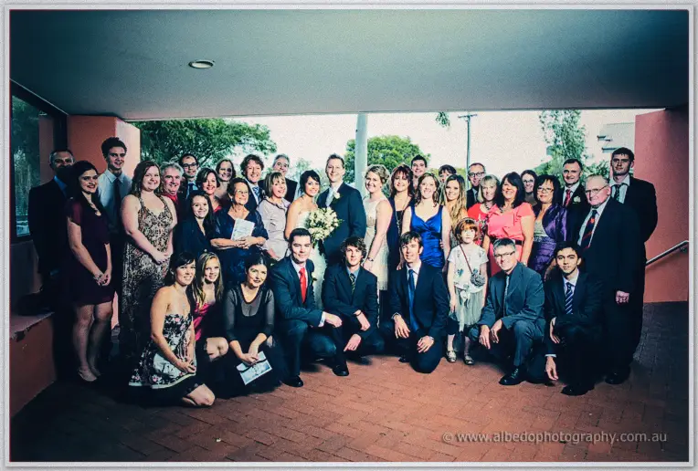 The whole wedding crowd gathers under a terracotta colonnade for a group portrait with the newlyweds