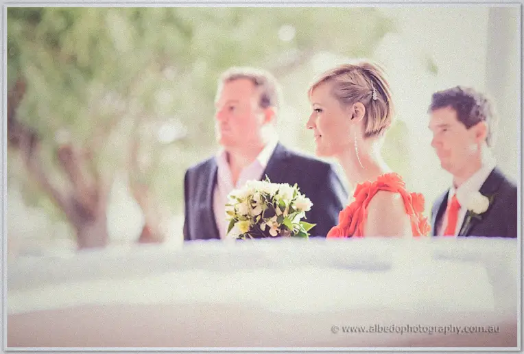 Soft-focus glimpse of guests in suits and a red dress chatting over white bouquets outside