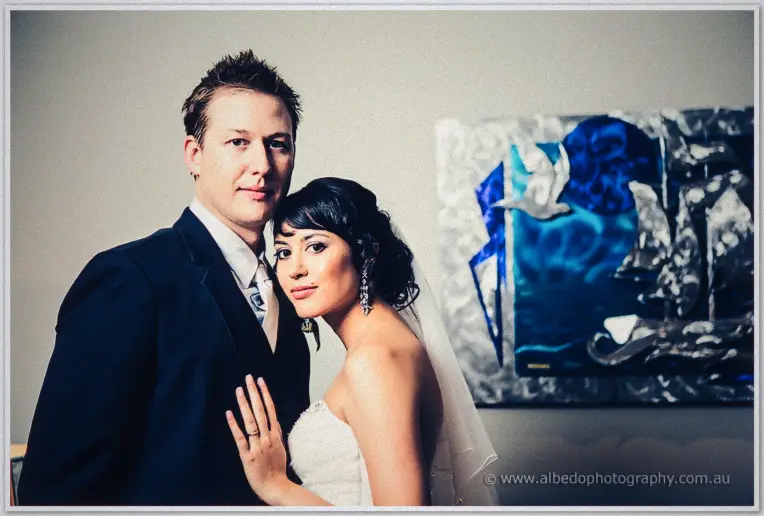 The couple lean together facing the camera, Sarah's ring hand raised, blue artwork glowing behind
