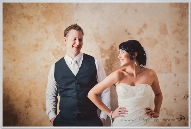 Sarah looks up laughing at Shannon as they pose casually against the mottled ochre wall