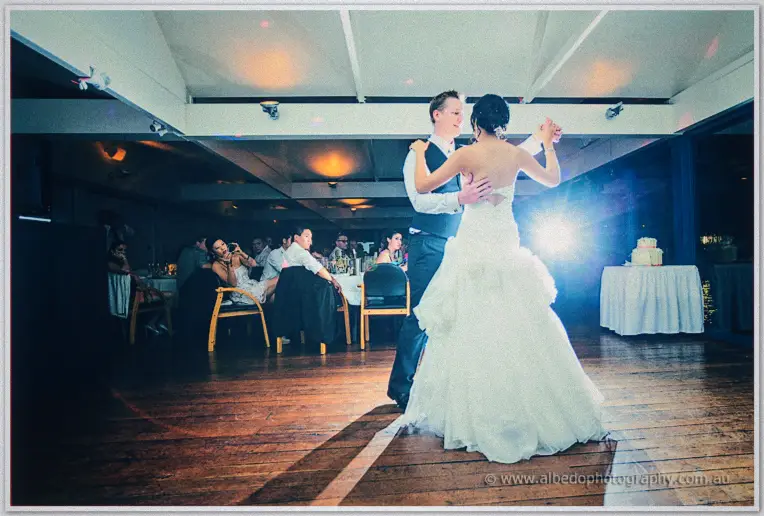 Sarah and Shannon sway cheek to cheek, camera flare blazing behind them past seated guests