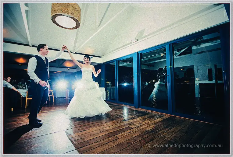 Shannon twirls Sarah beneath a woven pendant lamp, night reflections in the glass walls