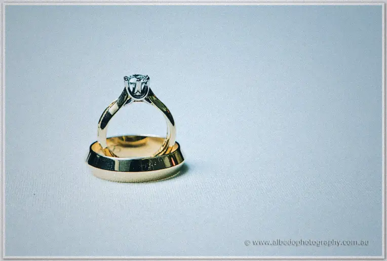 Diamond solitaire engagement ring resting on a plain gold wedding band in soft pale light
