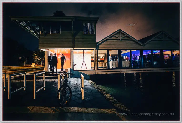 Night falls over the glassed waterside function room, guests inside and a bike by the jetty entrance