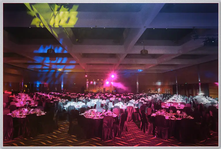Ballroom of round dinner tables washed in pink and blue stage light at the 2012 catering awards night