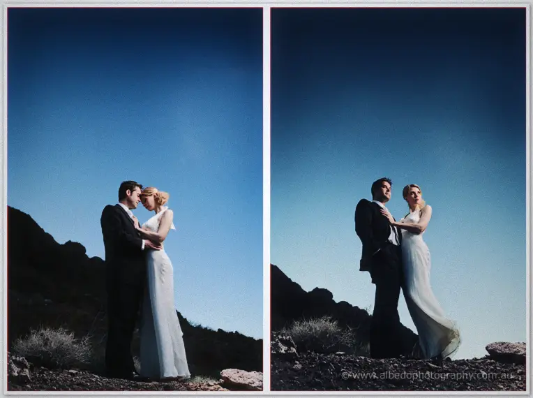 Couple embraces on rocky desert ground beneath a huge deepening blue evening sky