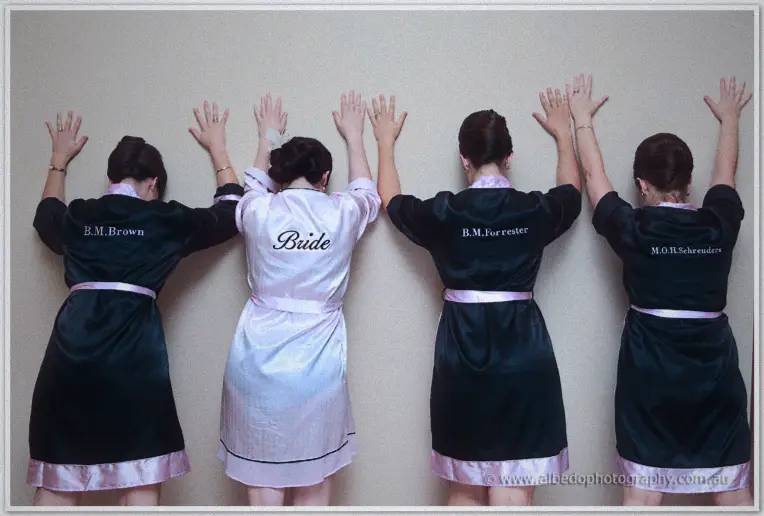 Bride and bridesmaids pressed hands to the wall showing embroidered robe backs