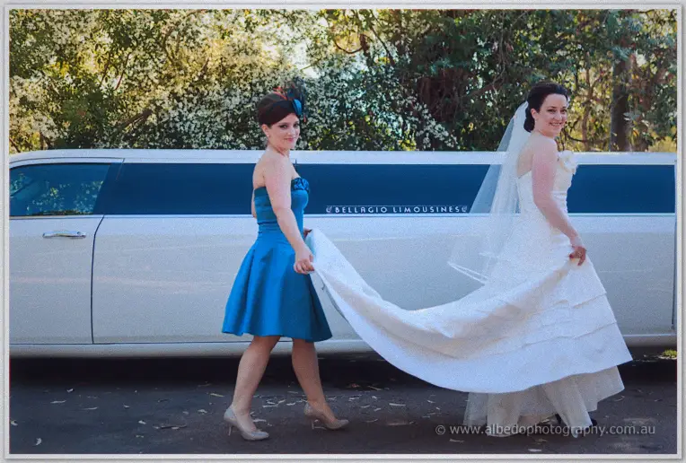 Bridesmaid carrying Felicity's train past a white stretch limousine