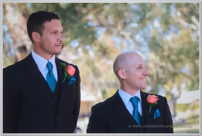 Groom Phil and his groomsman waiting in black suits with teal ties and coral roses