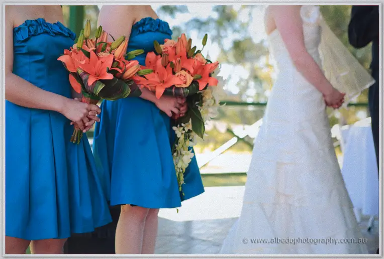 Bridesmaids in blue dresses holding coral lily bouquets beside the bride