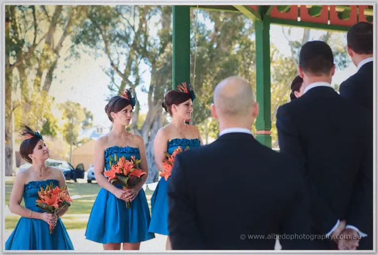Bridesmaids with feathered headpieces listening as Phil says his vows