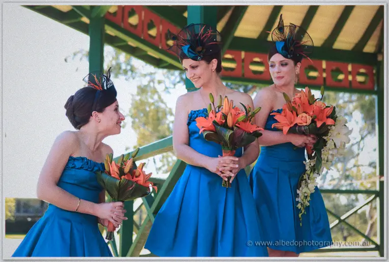 Bridesmaids in blue sharing a joke under the gazebo's green beams