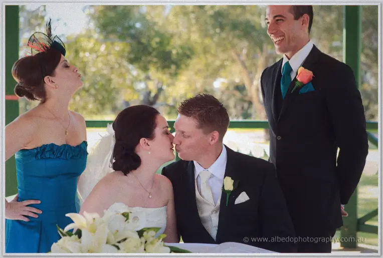 The couple kissing over the register as their bridal party laughs