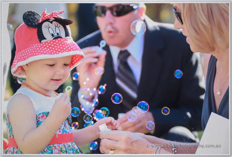 Toddler in a polka-dot sun hat blowing bubbles among the guests