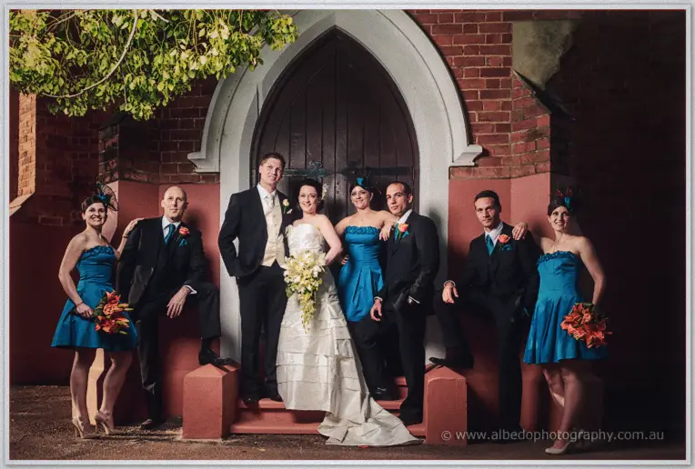 Full bridal party grouped on the church steps beneath the arched door