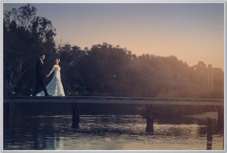 Felicity and Phil stroll hand in hand down the jetty in hazy golden light after their ceremony