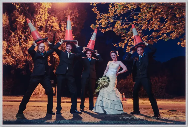 Groomsmen balance orange traffic cones on their heads as Felicity laughs with her bouquet