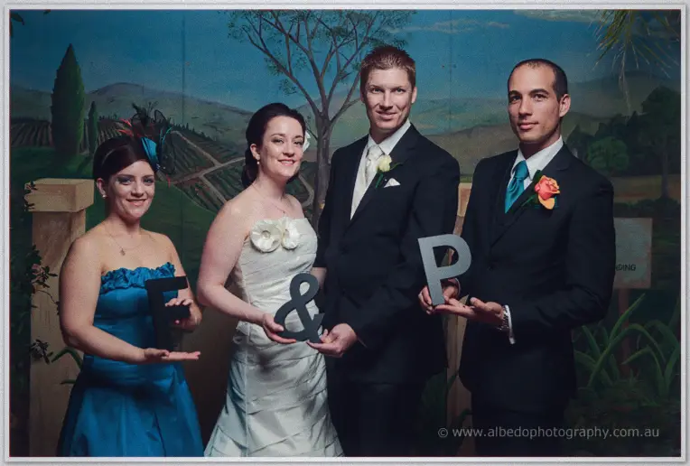 Felicity and Phil join wedding guests holding letter props in a photo booth at their reception