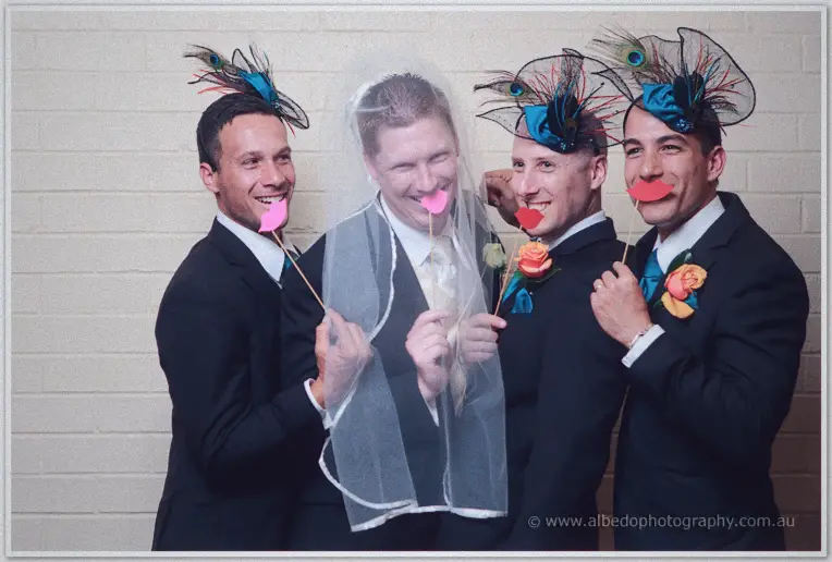 Phil wears the bridal veil as groomsmen in feather fascinators hold paper lips, all laughing