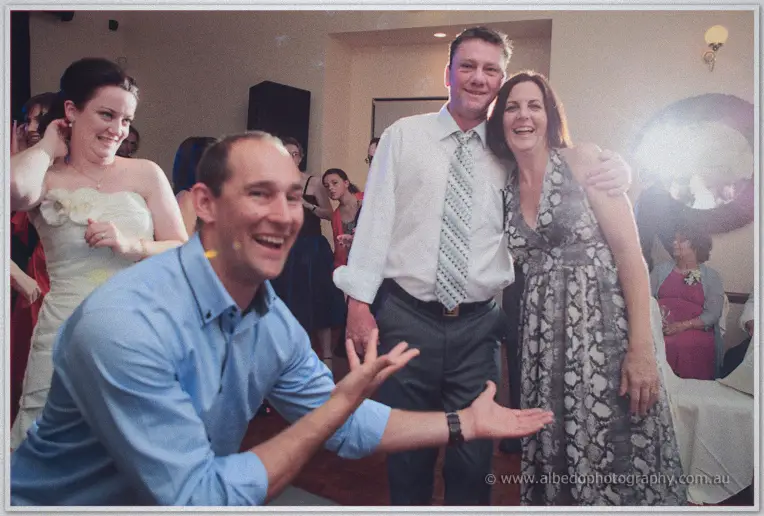 A guest throws his arms wide in laughter as dancers fill the reception floor behind him