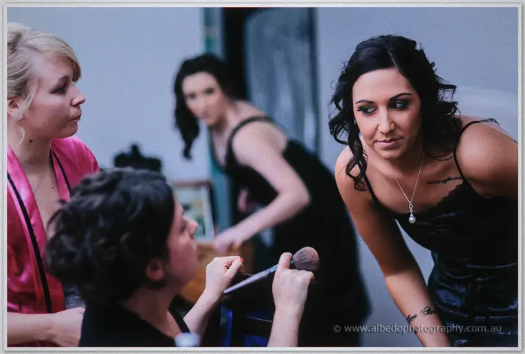 A bridesmaid leans in as the makeup artist powders a seated member of the bridal party