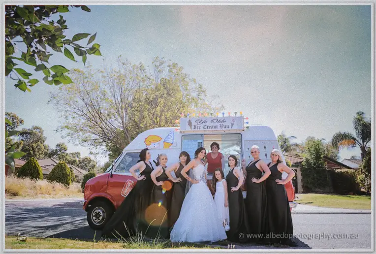 The bridal party in navy gowns gathers on the grass around Jenna and the vintage ice cream van