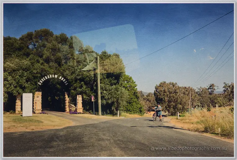 A cyclist rides past the Caversham House entrance arch beneath a clear blue sky