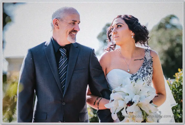 Jenna beams up at her father as he walks her down the aisle clutching white lilies