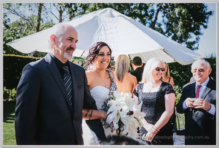 Jenna smiles beside her father under a garden umbrella as guests turn to watch