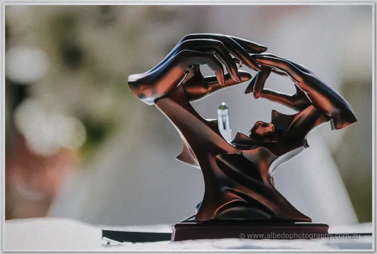 A bronze sculpture of cradling hands holds the wedding rings in soft garden light