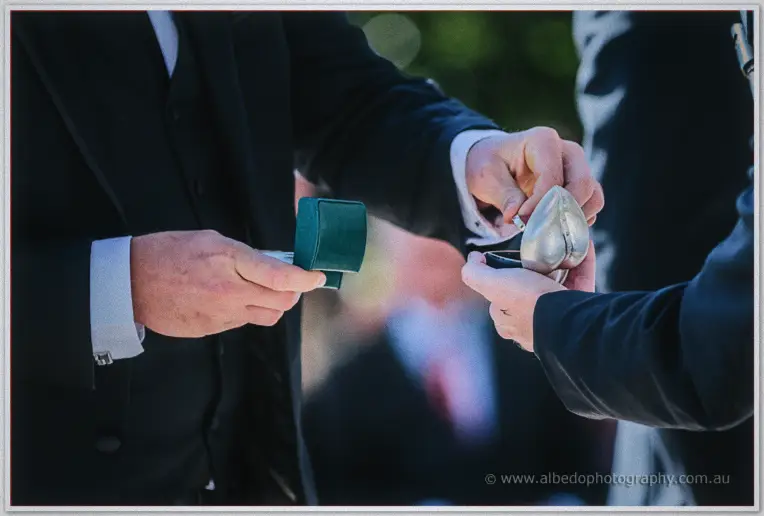 A groomsman passes a heart-shaped silver box to Andrew during the ring exchange