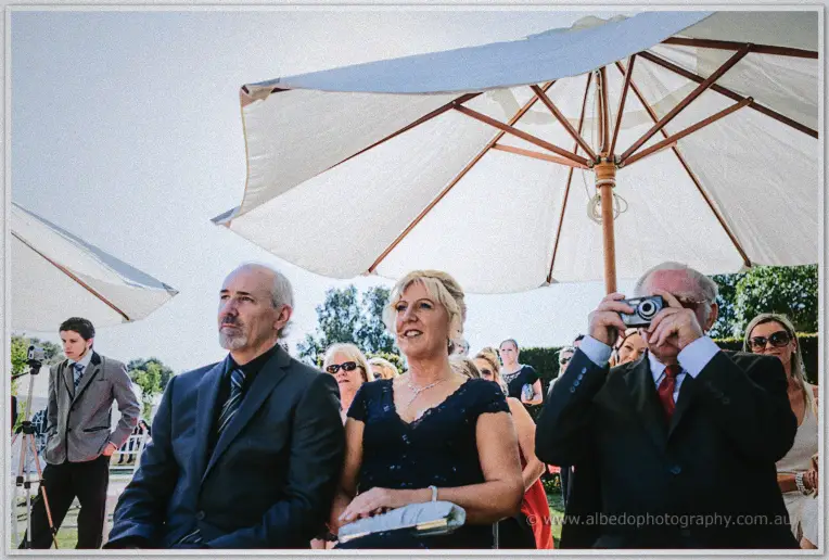 Wedding guests under a white market umbrella, one man shooting pictures with a compact camera