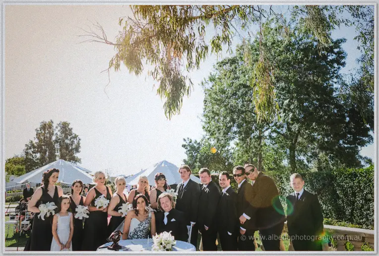 The full bridal party gathers around the seated couple for a group portrait under the gum trees