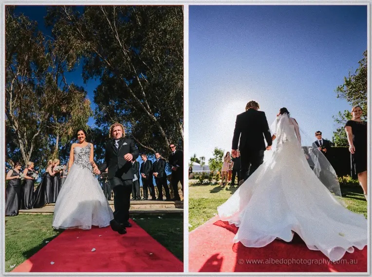 The newlyweds walk the red carpet past their smiling bridal party under a deep blue sky