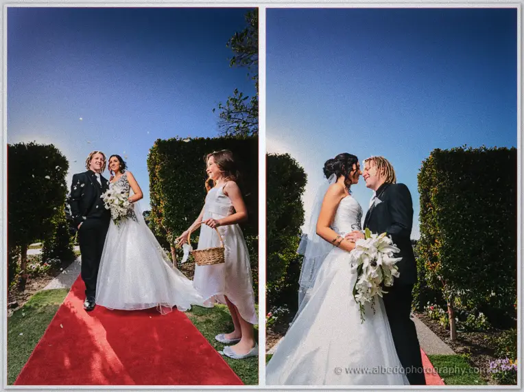 A flower girl scatters petals down the red carpet as the couple turns to kiss among the hedges
