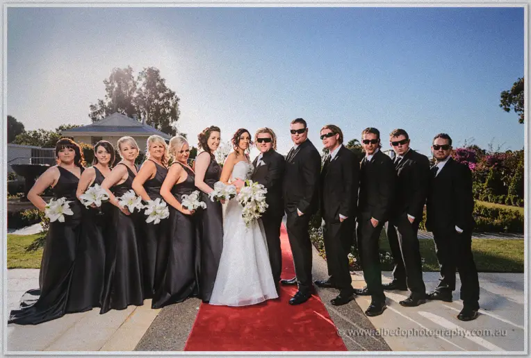 Jenna and Andrew front their sunglasses-clad bridal party lined along the red carpet