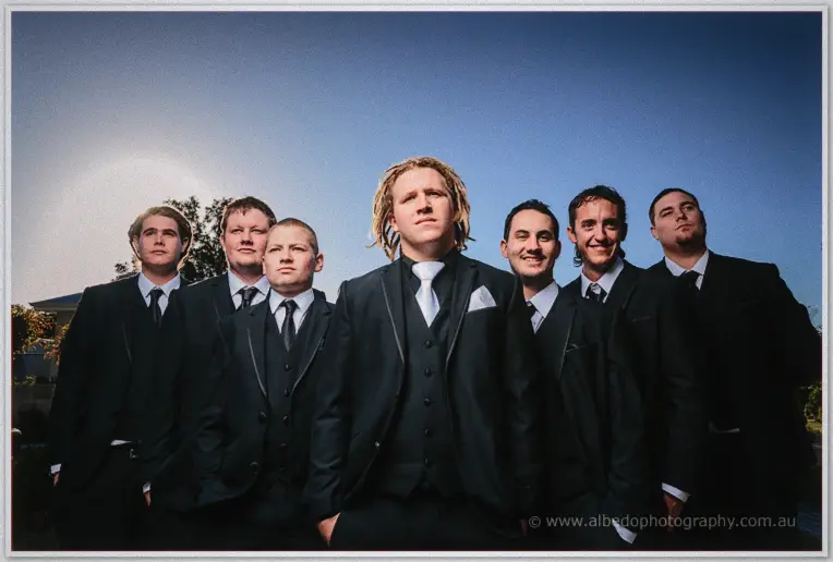 Andrew fronts his groomsmen in a low-angle portrait against a washed blue sky